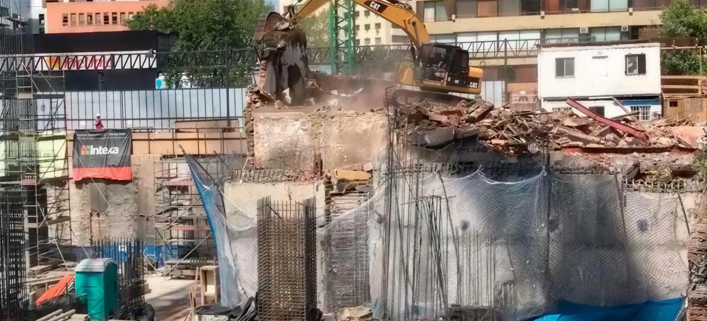 Excavadora demoliendo la estructura de un edificio tras malla de protección